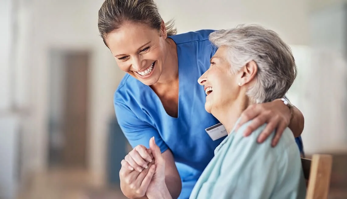 Caregiver in blue scrubs assisting an older woman at home